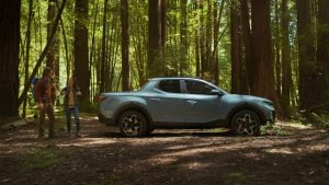 A light blue 2022 Hyundai Santa Cruz in the woods with two hikers.
